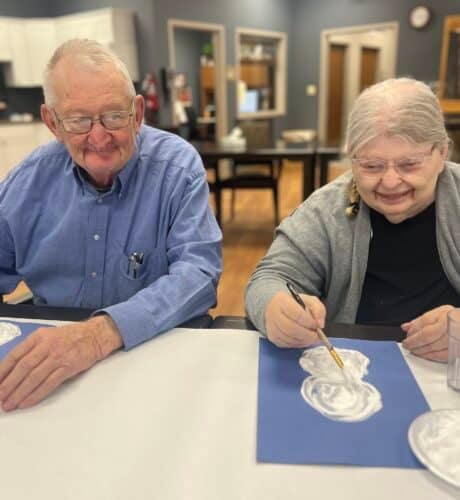 two elders sitting at a table painting